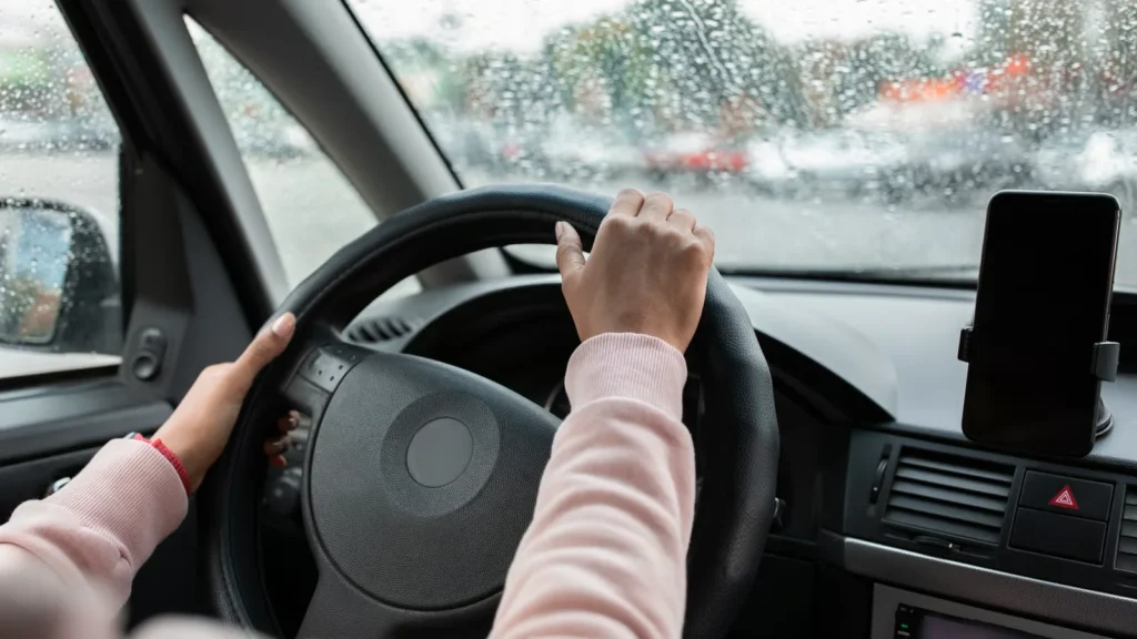 Driver safely traveling on a rainy United States road while maintaining distance and using headlights in bad weather.